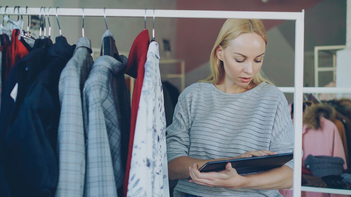 Store associate reviewing stock on a tablet beside a clothing rail
