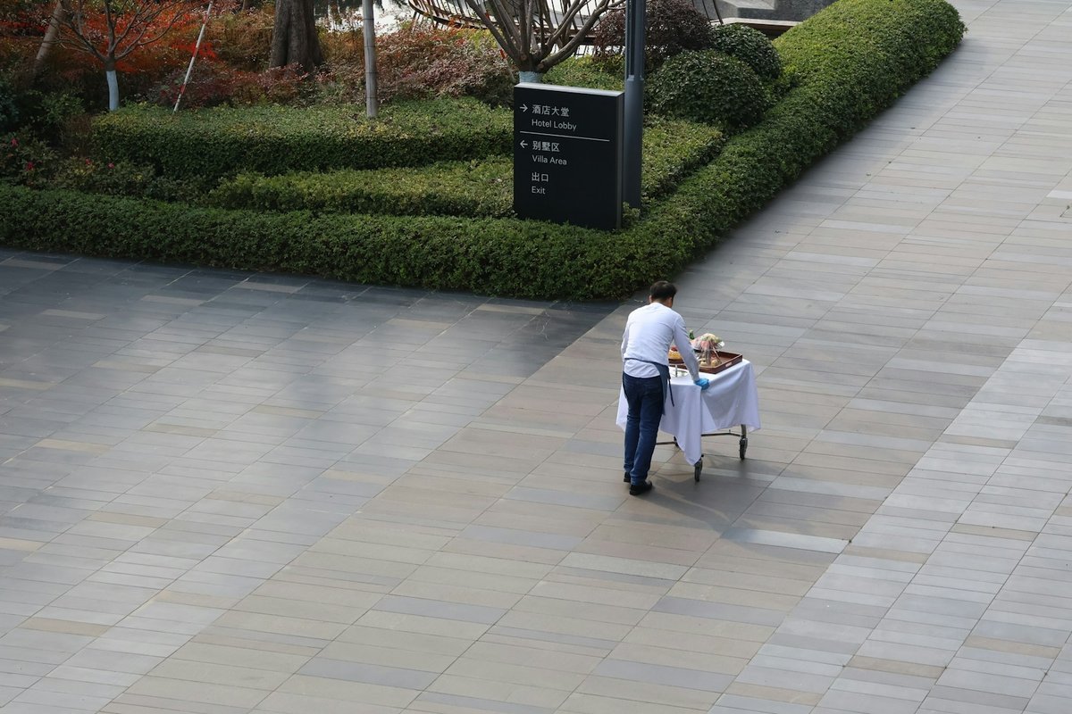 Hotel attendant moving a service trolley along a garden walkway between the lobby and villas