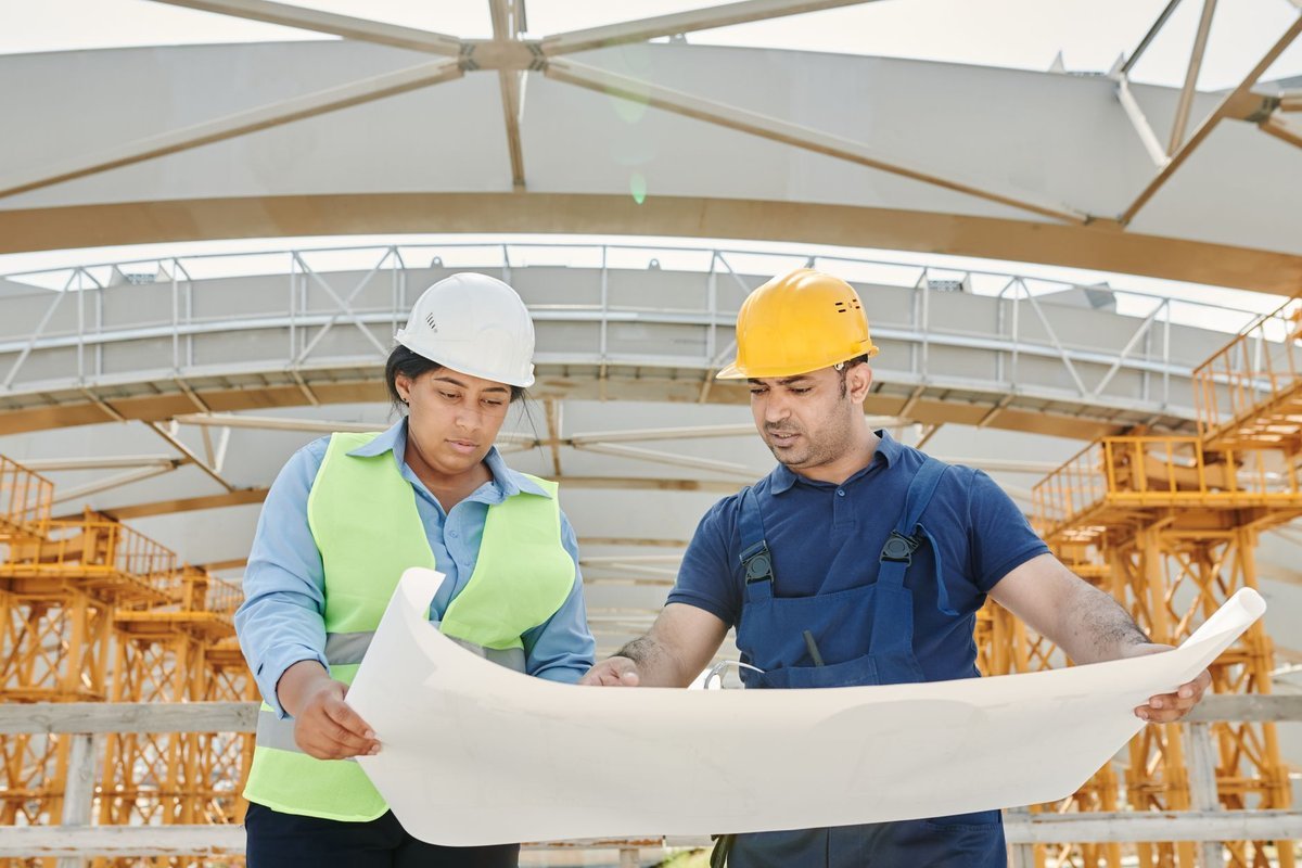 Two site engineers in hard hats reviewing drawings on a construction site
