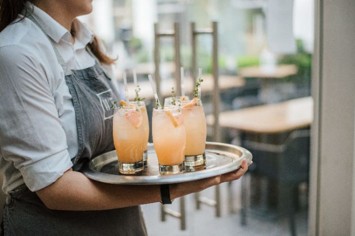 Hospitality server presenting craft cocktails on a tray