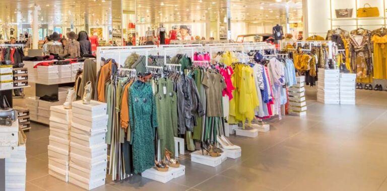 Racks of apparel and shoes in a brightly lit clothing store.