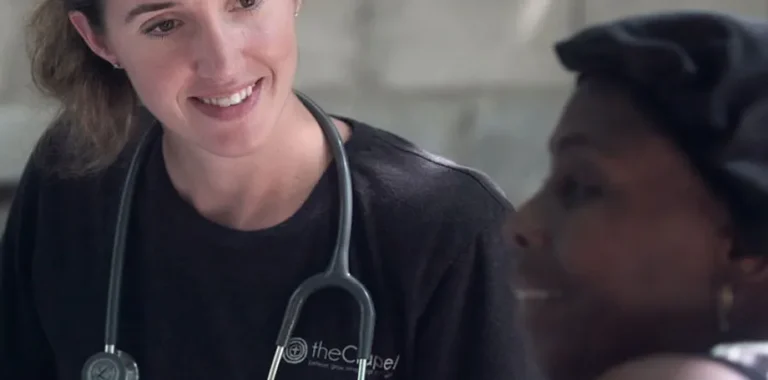 Smiling healthcare worker with stethoscope looks at another woman.