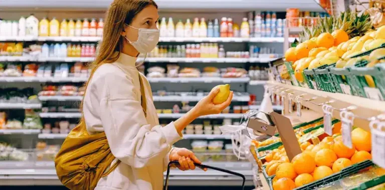 Masked woman choosing a lemon in a grocery store.