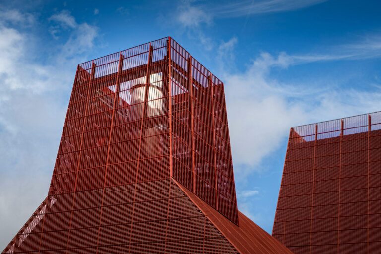 Red modern building with perforated facade against blue sky.