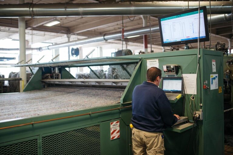 Worker operating textile carding machine using computers.