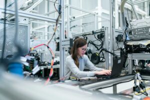 Woman engineer using laptop in automotive testing facility.
