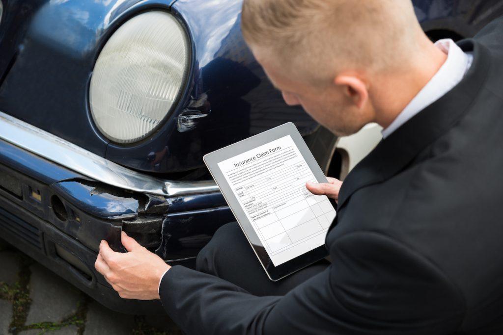 Man inspecting damaged car and filling digital insurance claim.
