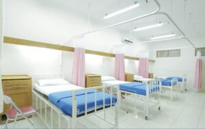 Hospital ward with several beds and privacy curtains.