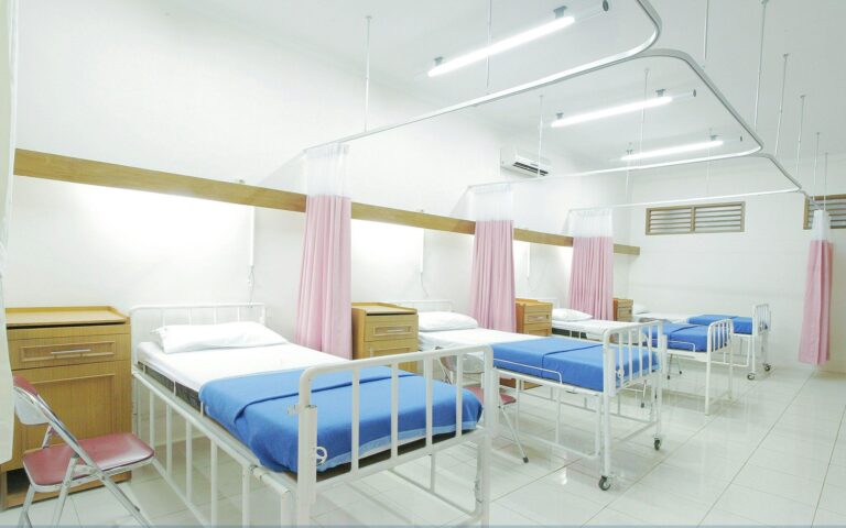 Hospital ward with several beds and privacy curtains.