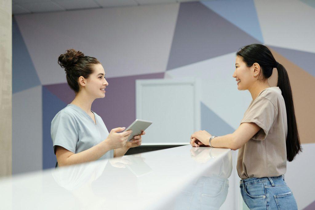 Medical receptionist assists smiling patient at front desk.