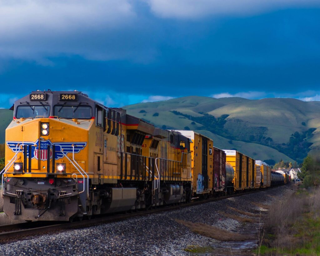 Yellow Union Pacific freight train on tracks, rolling green hills background.