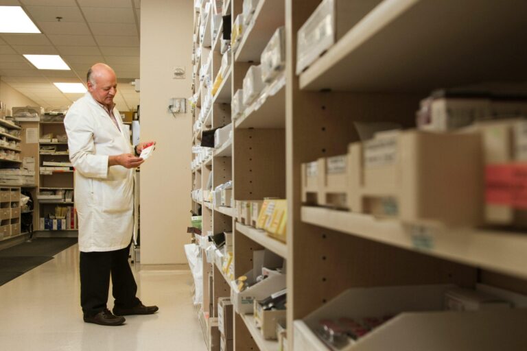 Pharmacist examining medication in a pharmacy supply room.