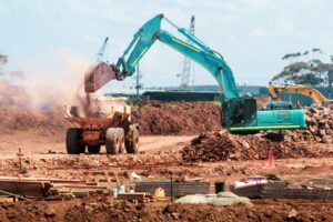 Turquoise excavator loads soil into a yellow dump truck.