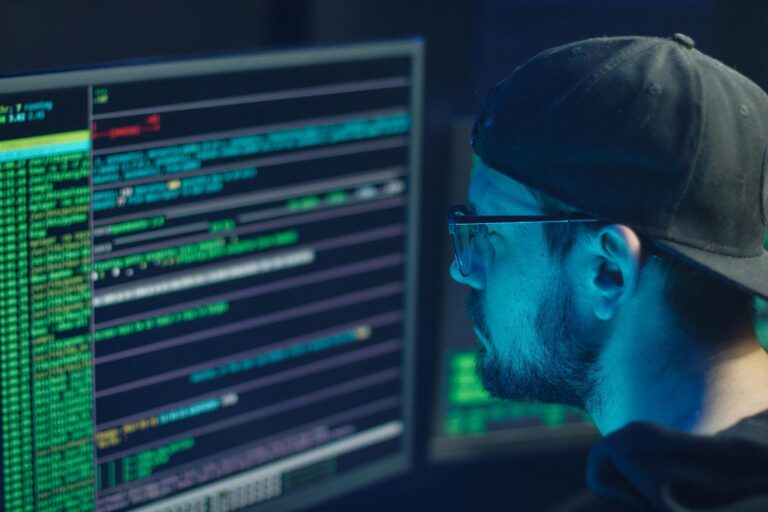 Man in cap and glasses watching glowing computer code.