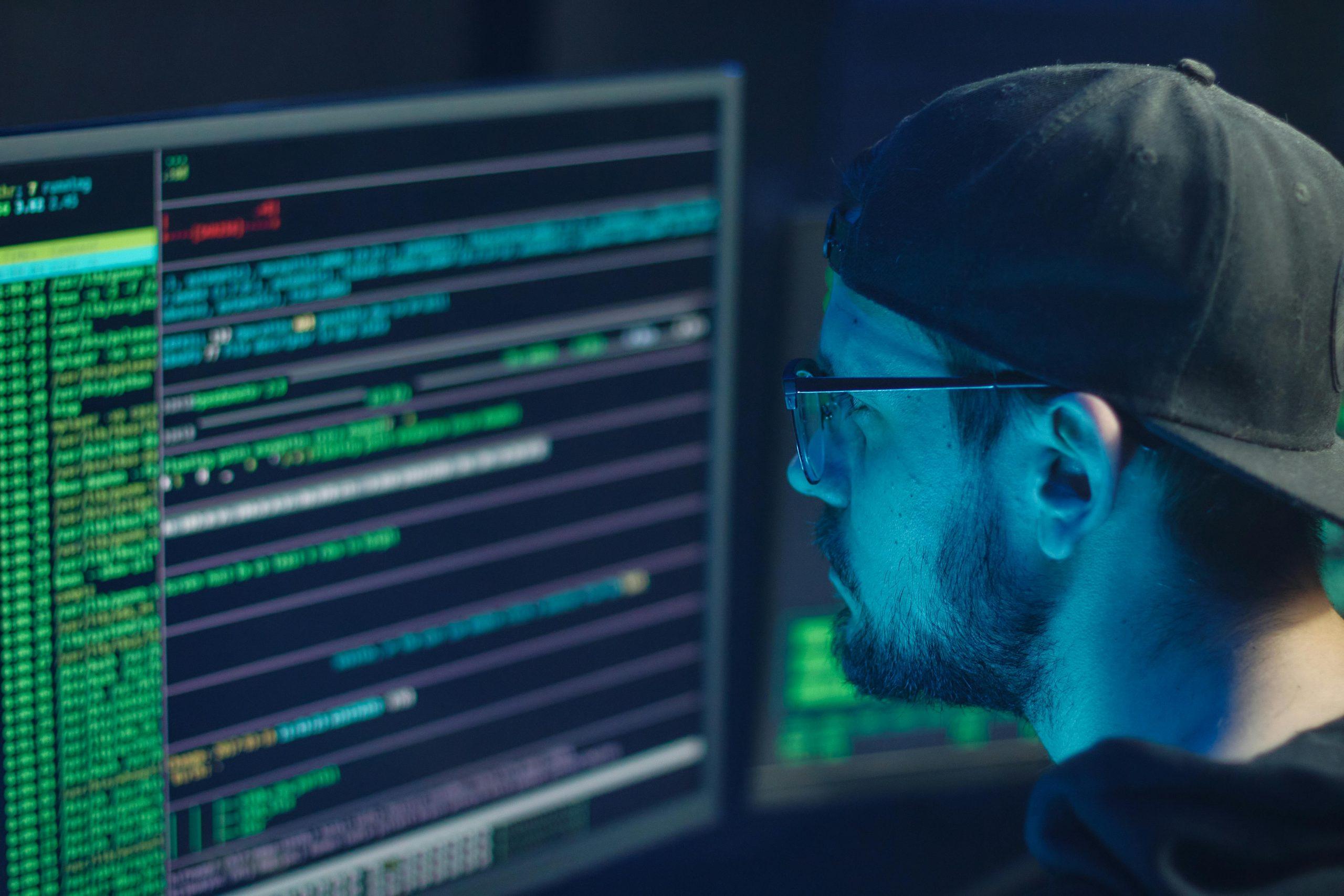 Man in cap and glasses watching glowing computer code.