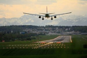 Jet airplane landing on illuminated runway with distant mountains.