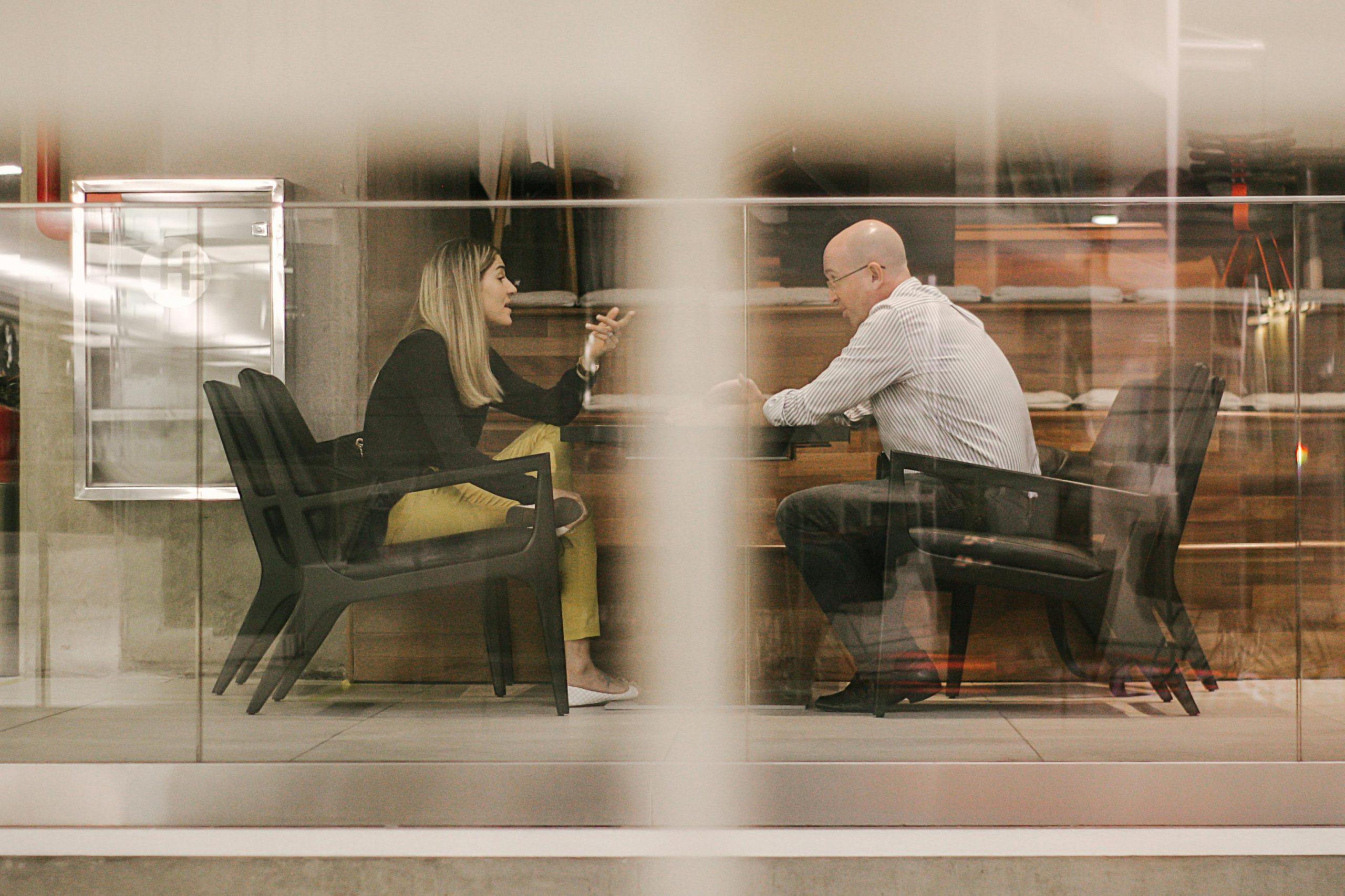 Woman and man conversing, viewed through glass.