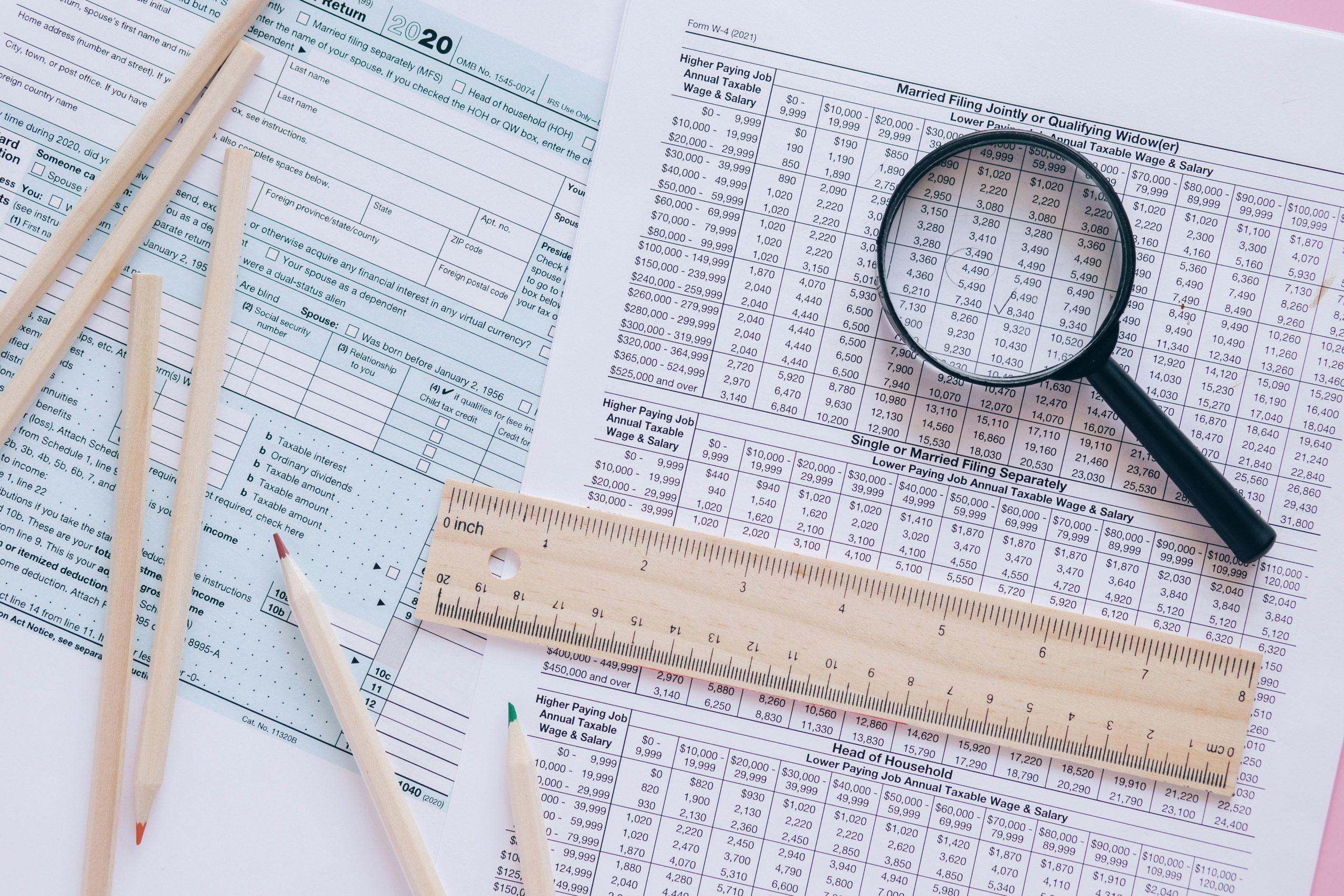 Tax forms, pencils, ruler, and magnifying glass for tax preparation.