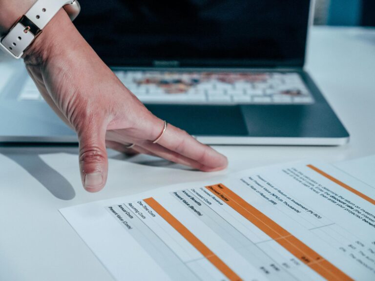 Persons hand reviewing financial document with laptop.