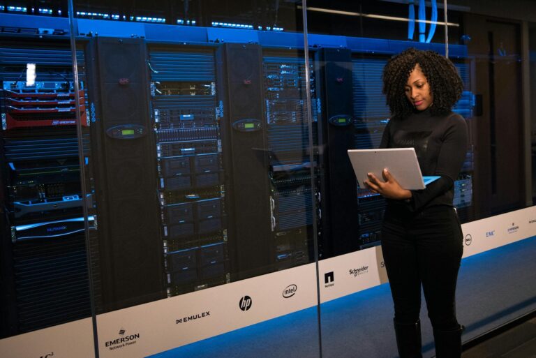 Woman reviewing data in a blue-lit server room.