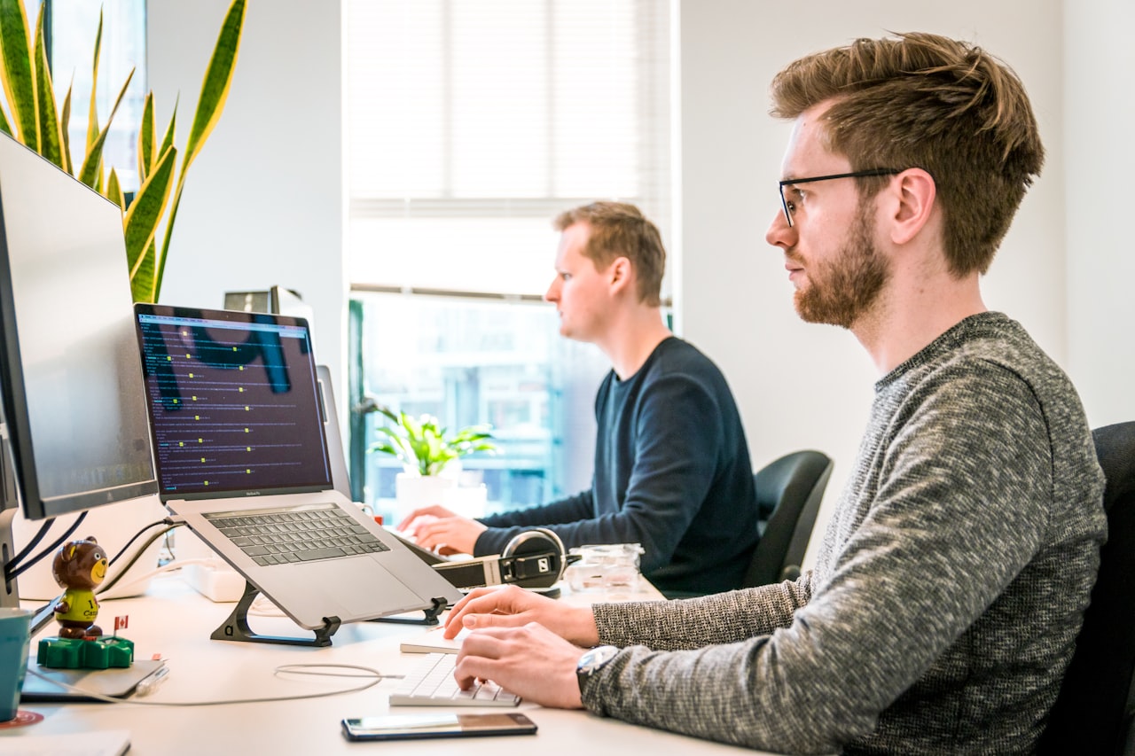 Two software engineers working at adjacent desks with code on screen