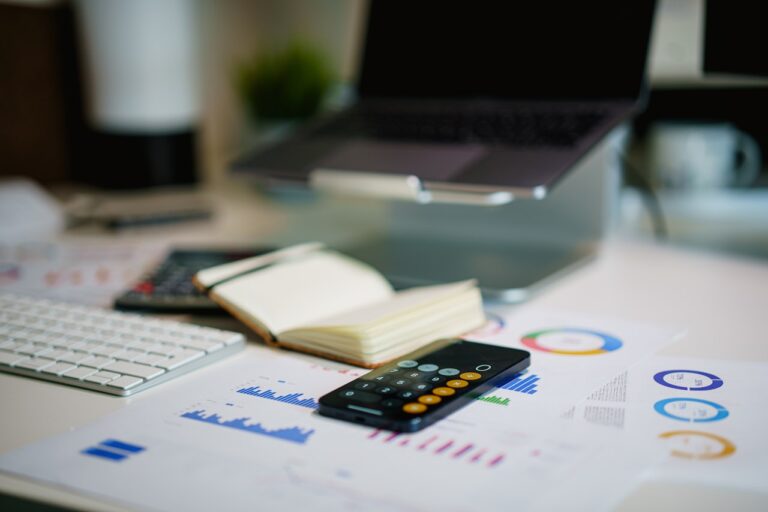 Office desk with printed financial charts, a calculator, and a laptop