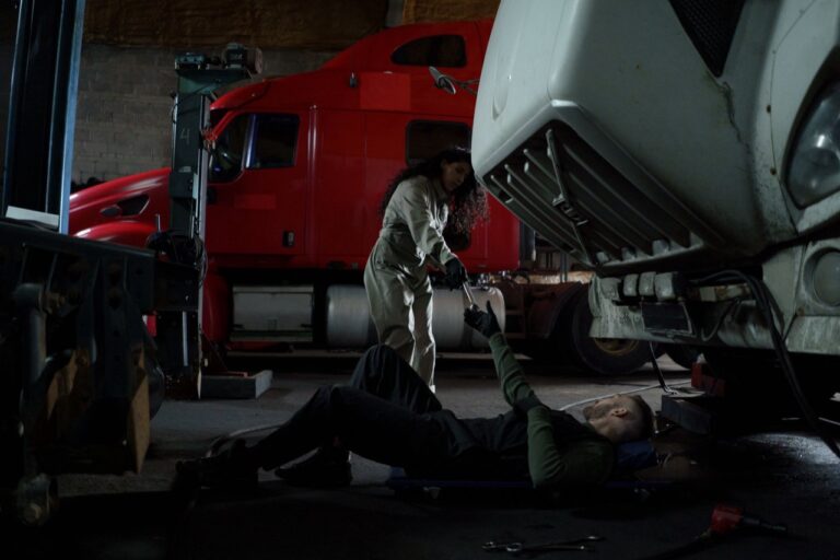 Two technicians servicing a heavy truck raised on a lift in a fleet maintenance garage