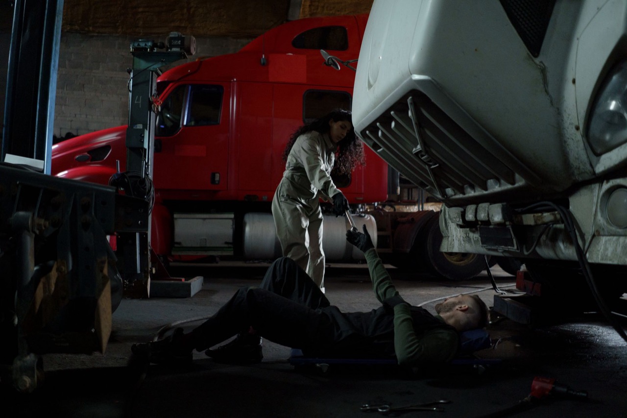 Two technicians servicing a heavy truck raised on a lift in a fleet maintenance garage