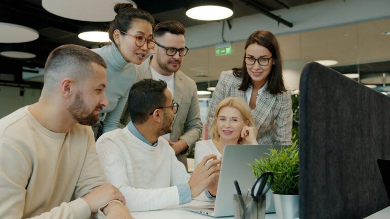 Small team gathered around a laptop in an open office, reviewing work together